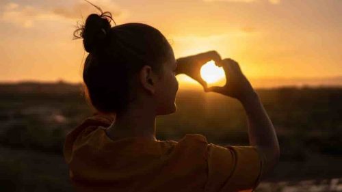 girl showing love sign with her fingers against the sun