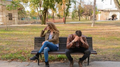 a couple sitting on a bench not talking to each other