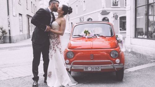 a newly married couple kissing near a red car